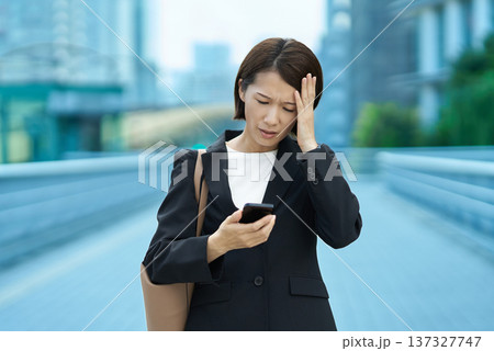 スマートフォンを手に不安な表情のビジネスウーマン スマートフォンを手に不安な表情のビジネスウーマン 137327747