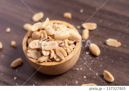 Peanuts in a wooden cup rest on a natural wood floor, creating a warm and rustic food-themed scene. 137327805