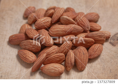Almonds arranged on a natural wood plate, showcasing their organic texture in a warm, simple setting. 137327809