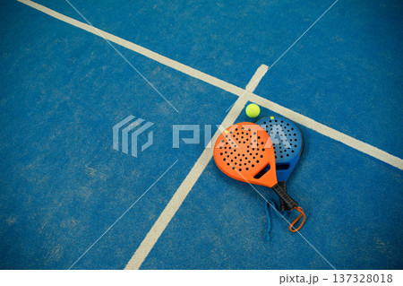 Padel paddles and a ball rest on the blue court surface Padel paddles and a ball rest on the blue court surface 137328018