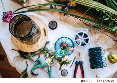 Top view of florist workspace features pruning shears and wire cutters next to flower frog and floral stems. Floral workshop, small business entrepreneur, creative workspace, floristry masterclass Top view of florist workspace features pruning shears and wire cutters next to flower frog and floral stems. Floral workshop, small business entrepreneur, creative workspace, floristry masterclass 137328039