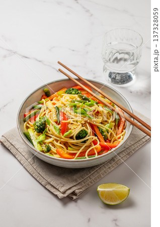 Vegetarian wok noodles with vegetables in a plate on a light marble background with chopsticks Vegetarian wok noodles with vegetables in a plate on a light marble background with chopsticks 137328059