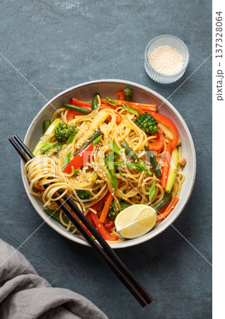 Stir fry wok noodles with vegetables in a plate on a dark background with chopsticks, sesame and napkin Stir fry wok noodles with vegetables in a plate on a dark background with chopsticks, sesame and napkin 137328064