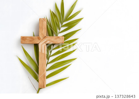 Simple wooden cross rests beside green palm fronds. Minimalist composition against clean white background. Natural textures highlight religious symbolism. Cross and leaves suggest themes of faith Simple wooden cross rests beside green palm fronds. Minimalist composition against clean white background. Natural textures highlight religious symbolism. Cross and leaves suggest themes of faith 137328643