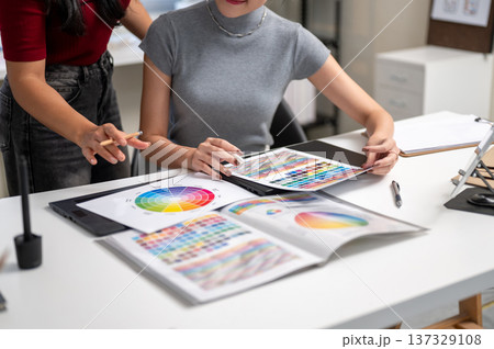 Close up of woman holding pencil explaining color to friend coworker at table in home office studio. Close up of woman holding pencil explaining color to friend coworker at table in home office studio. 137329108