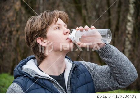 Sporty man drinking water from bottle at public park after workout. 137330438