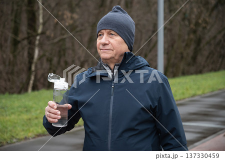 Sporty man drinking water from bottle at public park after workout. 137330459