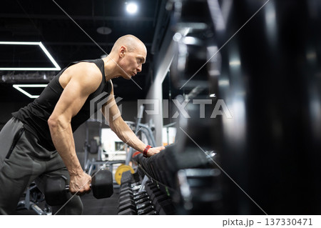 Strong athletic man doing one arm dumbbell row workout in modern gym Strong athletic man doing one arm dumbbell row workout in modern gym 137330471