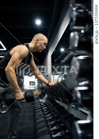 Strong athletic man doing one arm dumbbell row workout in modern gym Strong athletic man doing one arm dumbbell row workout in modern gym 137330484