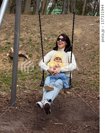 Mother holding baby on playground swing outdoors Mother holding baby on playground swing outdoors 137331944