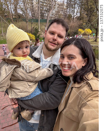 Happy family selfie in park with toddler wearing yellow beanie 137332075