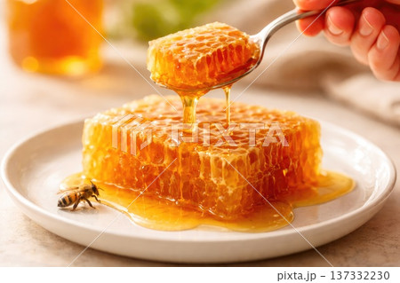 Honeycomb dripping with golden honey on spoon with bee closeup Honeycomb dripping with golden honey on spoon with bee closeup 137332230
