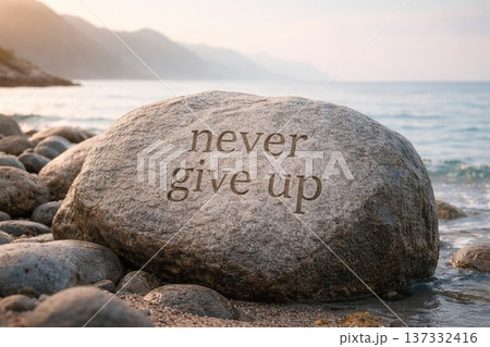 Engraved motivational quote never give up on large seaside stone with waves and mountains in background 137332416