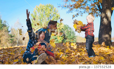 Happy family throwing colorful autumn leaves in the air at a park, enjoying a sunny fall day together Happy family throwing colorful autumn leaves in the air at a park, enjoying a sunny fall day together 137332528
