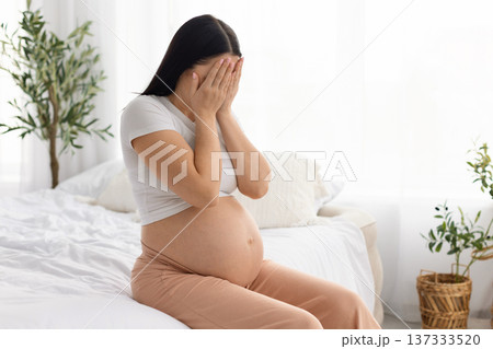 Pregnant woman sitting on bed covering face feeling emotional stress during pregnancy Pregnant woman sitting on bed covering face feeling emotional stress during pregnancy 137333520