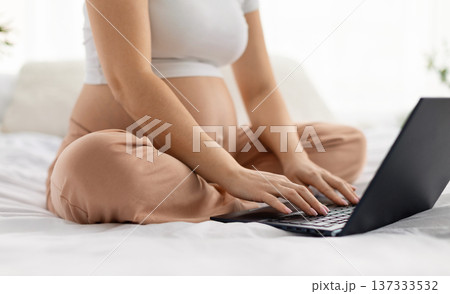 Pregnant woman sitting cross legged on bed using laptop at home 137333532