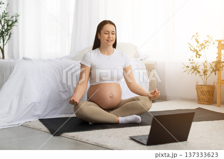 Pregnant young woman practicing prenatal yoga at home while watching laptop 137333623