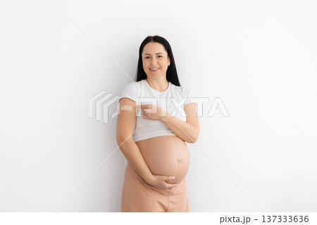 Pregnant woman pointing to vaccination bandage on arm while standing at home 137333636