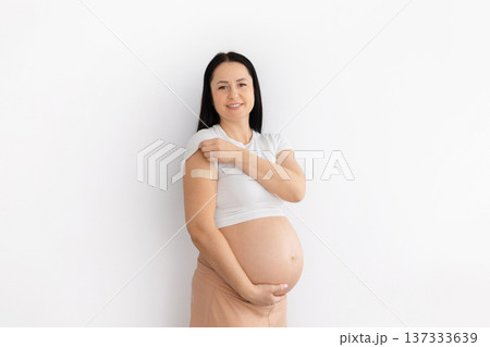 Pregnant young woman showing vaccination bandage on arm at home Pregnant young woman showing vaccination bandage on arm at home 137333639