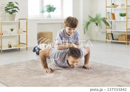 Athletic father doing push ups at home with cheerful son on his back enjoying fun family workout. 137333842