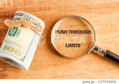 Magnifying lens on Push Through Limits wood, beside twine-bound US hundred dollar bills. Represents ambition financial ascent Magnifying lens on Push Through Limits wood, beside twine-bound US hundred dollar bills. Represents ambition financial ascent 137333850