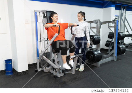 Mature woman training chest muscles with personal instructor Mature woman training chest muscles with personal instructor 137334132