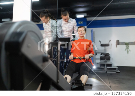Senior woman exercising on rowing machine with trainer 137334150
