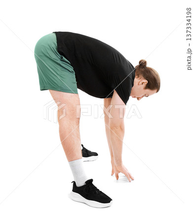 Sporty young man with long hair stretching his hamstrings by bending forward to touch the floor. Athletic male in green shorts isolated on white background. High quality photo Sporty young man with long hair stretching his hamstrings by bending forward to touch the floor. Athletic male in green shorts isolated on white background. High quality photo 137334198