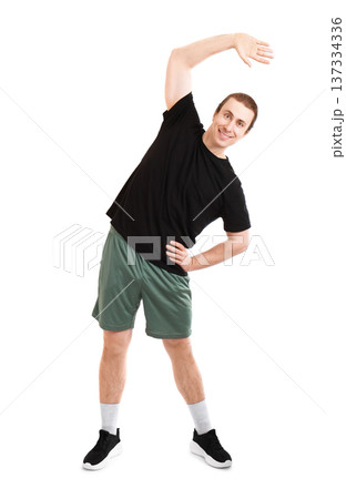 Smiling young sporty man doing side bend stretching exercise isolated on white background. Full body shot of a male athlete performing a fitness warm-up routine. High quality photo Smiling young sporty man doing side bend stretching exercise isolated on white background. Full body shot of a male athlete performing a fitness warm-up routine. High quality photo 137334336