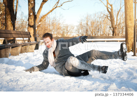 Young man slipping on ice and falling down in a snowy park. Winter accident, injury, and health insurance concept. Dangerous slippery road during a cold day. High quality photo 137334406