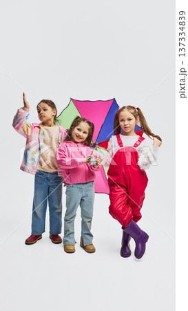 Three girls posing with colorful umbrella wearing mid season kids fashion outfits in studio. Three girls posing with colorful umbrella wearing mid season kids fashion outfits in studio. 137334839