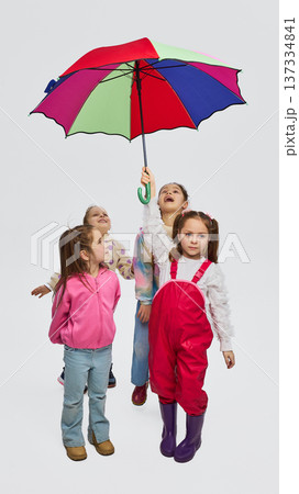 Girls under colorful umbrella wearing mid season rainwear kids fashion outfits in studio 137334841