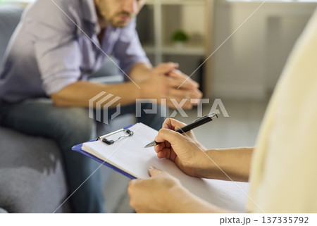 Therapist writing on clipboard as patient listens during private consultation 137335792