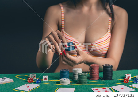 Woman Engaged in Card Game While Stacking Poker Chips on Green Felt Table with Dice and Playing Cards in a Casino Environment Woman Engaged in Card Game While Stacking Poker Chips on Green Felt Table with Dice and Playing Cards in a Casino Environment 137337133