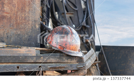 A hard hat sits on construction equipment while workers focus on tasks around the site. Tools and machinery are visible in the background A hard hat sits on construction equipment while workers focus on tasks around the site. Tools and machinery are visible in the background 137337744