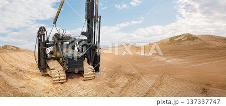 A pile driving rig operates in a sandy location under a blue sky with some clouds. The rig is preparing for construction work in the area A pile driving rig operates in a sandy location under a blue sky with some clouds. The rig is preparing for construction work in the area 137337747