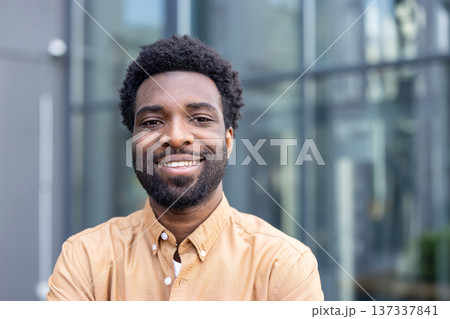 Young businessman with afro hairstyle smiling confidently outdoors in an urban setting, smart-casual and approachable, portrait conveying success, leadership and a bright future Young businessman with afro hairstyle smiling confidently outdoors in an urban setting, smart-casual and approachable, portrait conveying success, leadership and a bright future 137337841