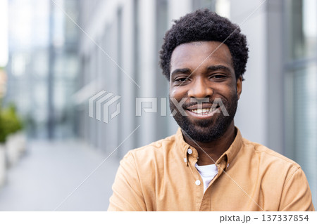 Confident young african person smiling brightly while standing outdoors in a city environment, expressing happiness and success with a friendly, welcoming demeanor 137337854
