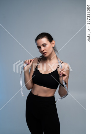 Young woman posing with a measuring tape around her neck, reflecting on her fitness success and commitment to a healthy lifestyle, symbolizing body goals and self-care 137338004