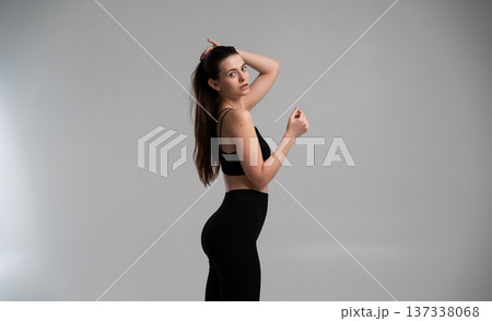 Attractive young woman with dark hair in activewear training, embodying fitness and health concepts, preparing for workout in studio on gray background 137338068