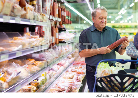 Mature man diligently choosing tasty sausage in supermarket Mature man diligently choosing tasty sausage in supermarket 137338473
