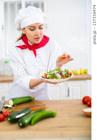 Smiling female chef in white uniform preparing vegetable salad in private kitchen 137338474