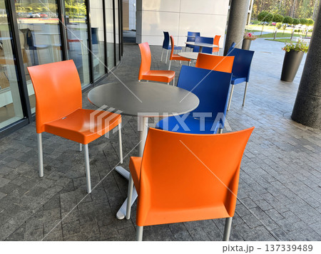 Orange and Blue Chairs and Round Tables in Street Cafe. 137339489