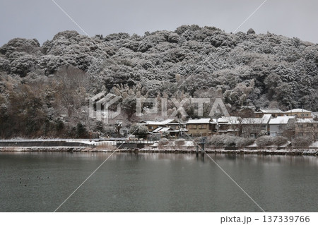 川と雪の積もる住宅街の町並みと山並みと冬空の風景 137339766