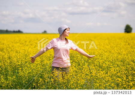 Young woman in bucket hat enjoying a warm summer day in blooming yellow rapeseed field under blue sky Young woman in bucket hat enjoying a warm summer day in blooming yellow rapeseed field under blue sky 137342013