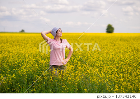 Woman in bucket hat raising arms up, enjoying a warm summer day in a blooming yellow rapeseed field Woman in bucket hat raising arms up, enjoying a warm summer day in a blooming yellow rapeseed field 137342140