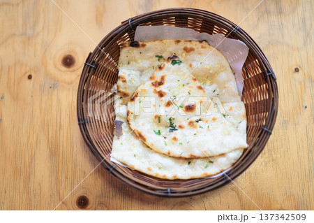 Top view of freshly baked garlic naan bread served in a wicker basket on a wooden table 137342509
