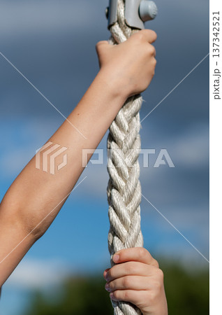 Teen boy hands holding rope against blue sky Teen boy hands holding rope against blue sky 137342521