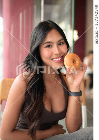 Smiling Woman Holding Glazed Donut in Cafe 137342549