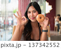 Young Woman Showing OK Gesture While Holding Glazed Donut in Cafe 137342552
